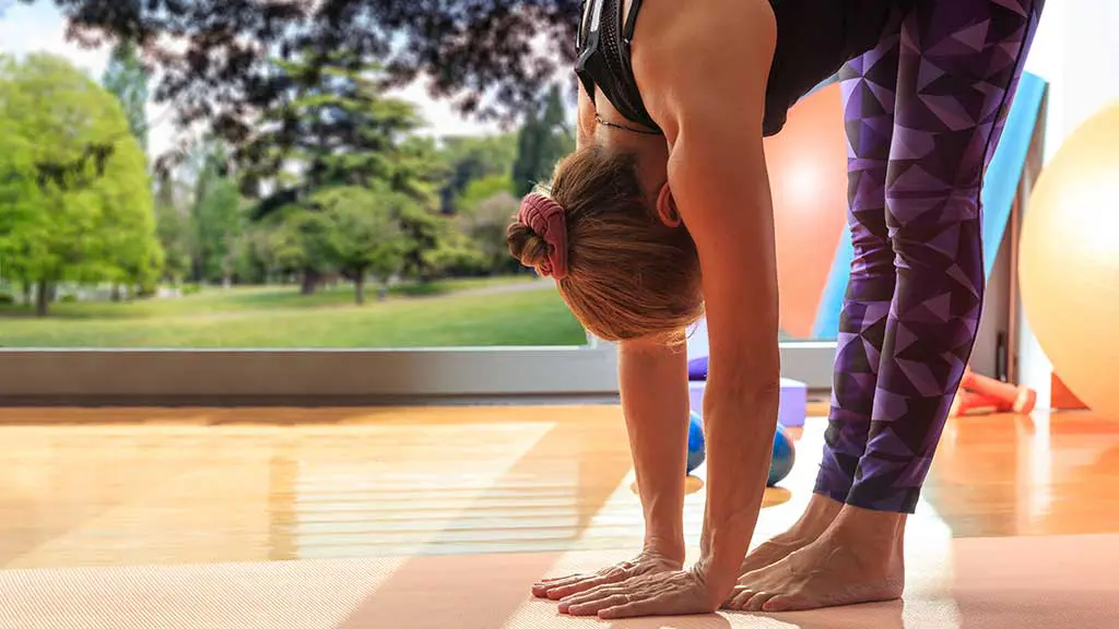 Frau macht bei einer Pilates Übung die Hände auf den Boden